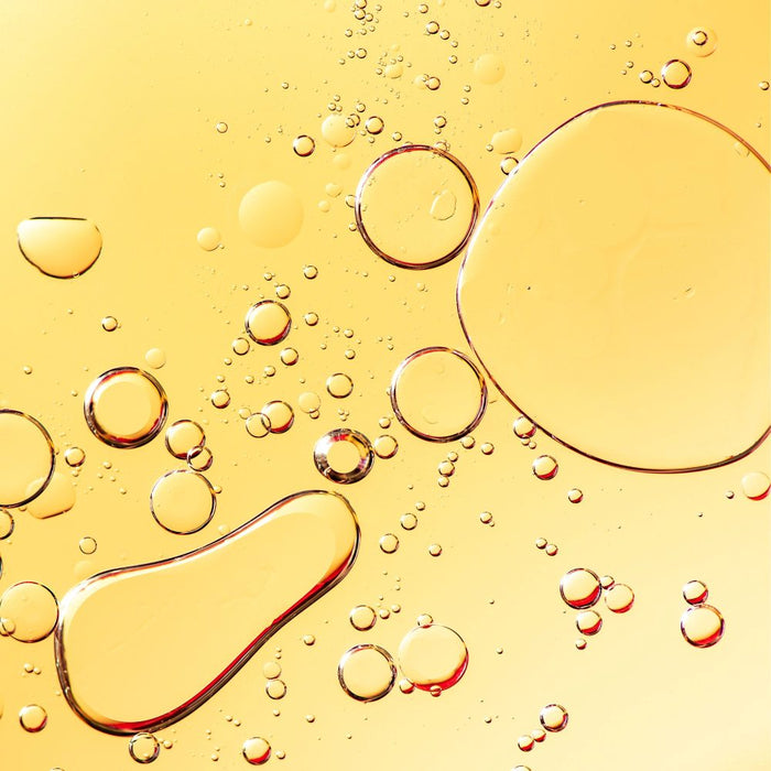 Close-up of oil bubbles on a yellow liquid surface representing jojoba oil