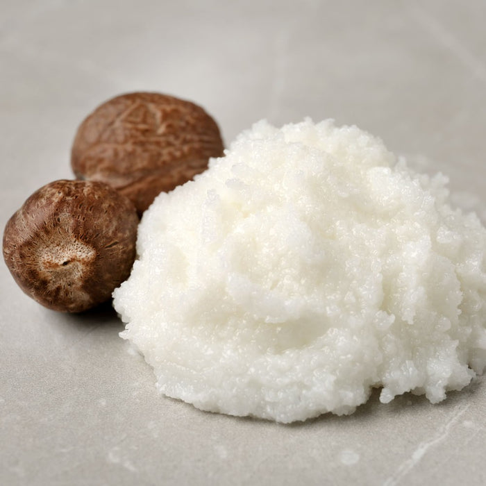 Coconut oil and two coconuts on a light gray surface representing shea butter